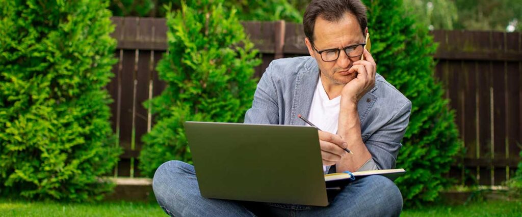 En-man-sitter-på-gräsplätten-med-sin-laptop-och-ser-fundersam-ut