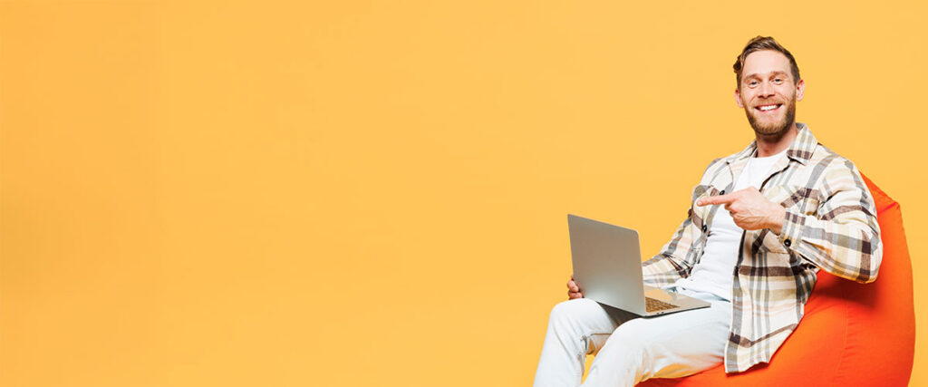 Person-sitter-med-laptop-och-pekar-åt-sidan-mot-gul-bakgrund